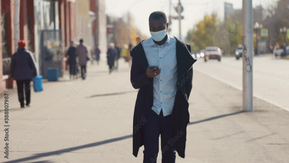 Portrait of African American business man in mask, smartphone in hands. City walk down the street during the coronavirus pandemic. Portrait of African American business man in mask, smartphone in hands. City walk down the street during the coronavirus pandemic.