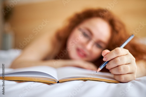 close-up photo of pen and diary, redhead female writing her plans, making notes with pen. on bed