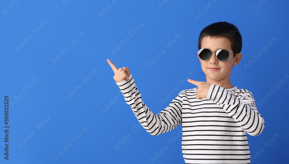Cute boy with stylish sunglasses pointing at something against color background Cute boy with stylish sunglasses pointing at something against color background