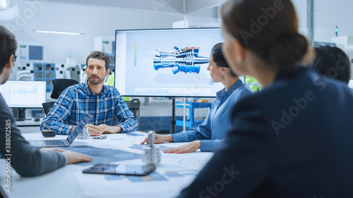 Modern Factory Office Meeting Room: Diverse Team of Engineers, Managers and Investors Talking at Conference Table, Use Interactive TV, Analyze Sustainable Energy Engine Blueprints. High-Tech Facility