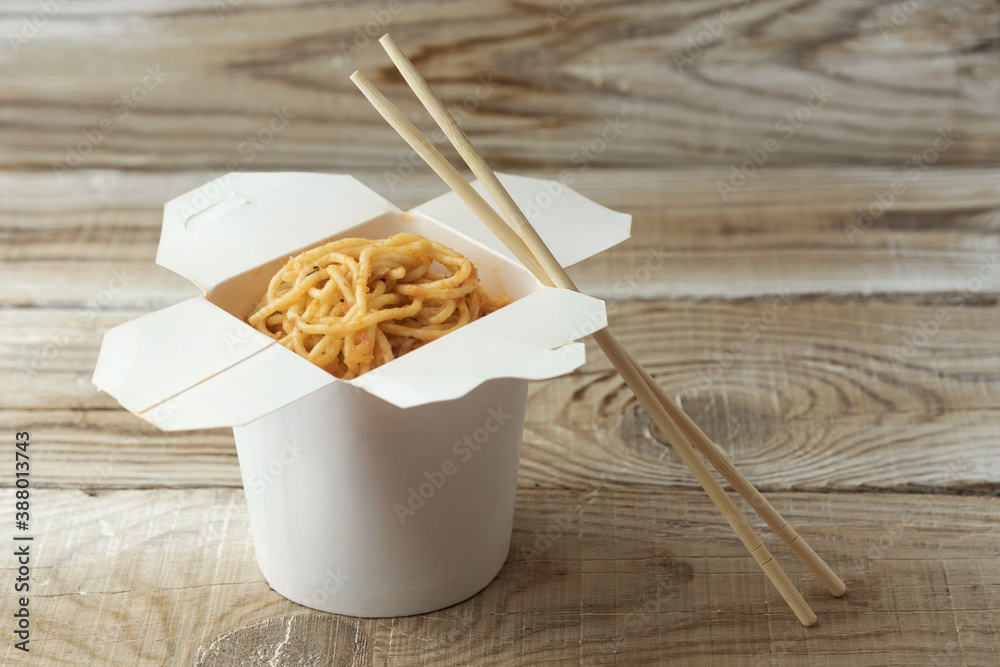 noodles in a box with sticks on a wooden background - obrazy, fototapety, plakaty 