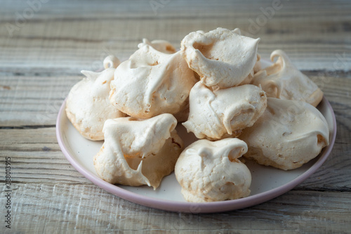 Homemade meringue cookies on a plate, on a wooden table by the window, closeup. Italian, French sweet dessert made of eggs and sugar, natural light.