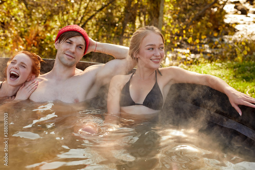 young caucasian friends taking bath jacuzzi outdoors, relaxed people in swimwear have fun, enjoy warm bath in the forest. relaxation, water recreation concept