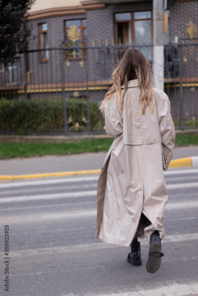 Fototapeta premium beautiful slim young brunette in fashionable trench coat and black dress cross a pedestrian crossing.