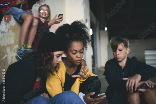 Konstfotografi Group of teenagers gang sitting indoors in abandoned building, using smartphones