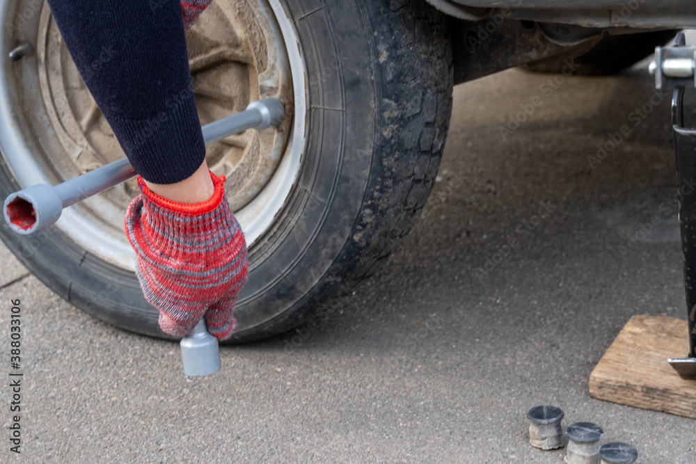 A woman with a wheel wrench unscrews a wheel from a car to replace it. A woman with a wheel wrench unscrews a wheel from a car to replace it.