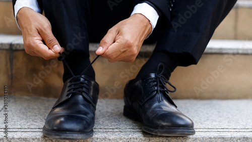 close up hand businessman in tie up shoelace on wearing leather shoes sitting staircase background. Men's style. 