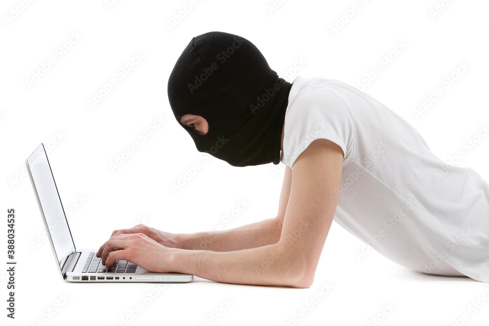 Young caucasian man with black balaclava helmet hacking a laptop. Studio photo. Young caucasian man with black balaclava helmet hacking a laptop. Studio photo.