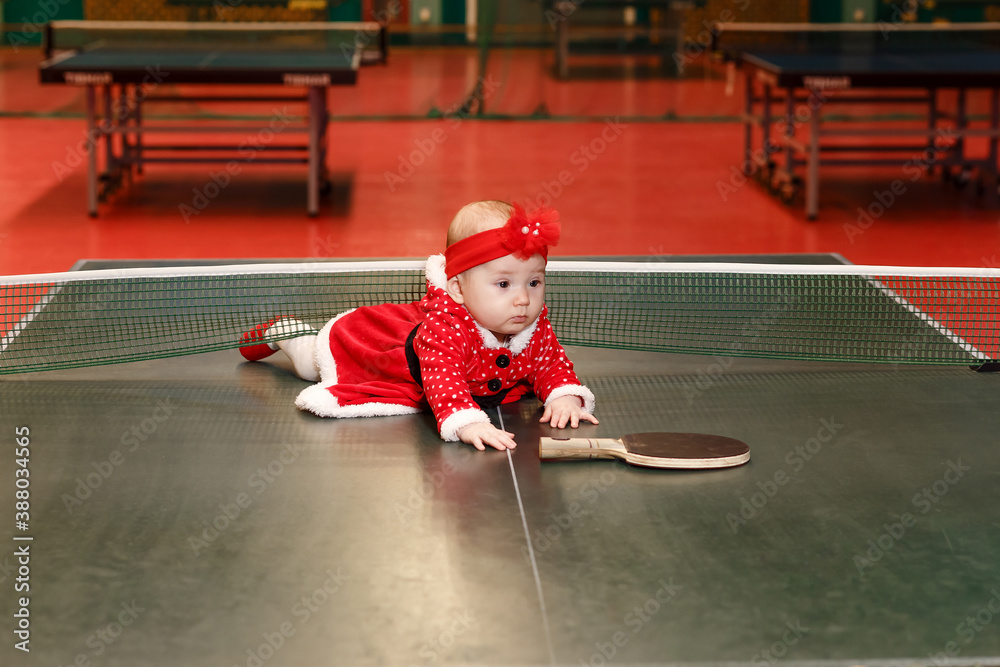 Φωτογραφία Six-month-old baby girl in a red Santa costume for Christmas at the tennis table with a racket