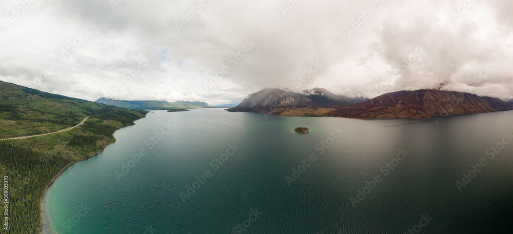 Beautiful Panoramic View of Lake alongside Scenic Road surrounded by Mountains and Trees on a Cloudy Day. Aerial Drone Shot. Taken near Klondike Highway, Southern Yukon, Canada.