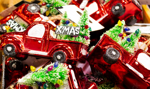 Close up a bunch of Christmas decorations in the form of a red cars trucks with a decorated Christmas tree in the back and the inscription Xmas