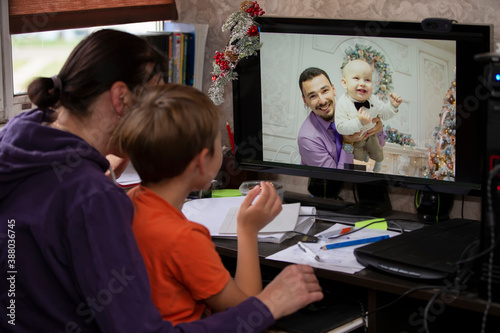 A woman and a child are sitting at a table and talking via video link with relatives or friends. Staying at home, quarantine and social distancing during the New Years.