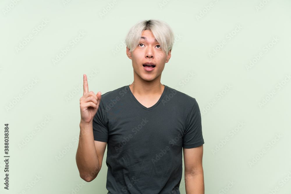 Young asian man over isolated green background pointing up and surprised Young asian man over isolated green background pointing up and surprised