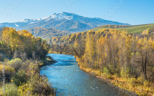 River, forested banks and a snow-capped peak. Sunny autumn day.