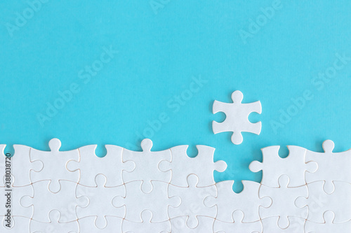 Assembling jigsaw puzzle pieces, Top view unfinished white jigsaw puzzle on blue background, Fragment of a folded white jigsaw puzzle with copy space, Teamwork and problem solving concept.