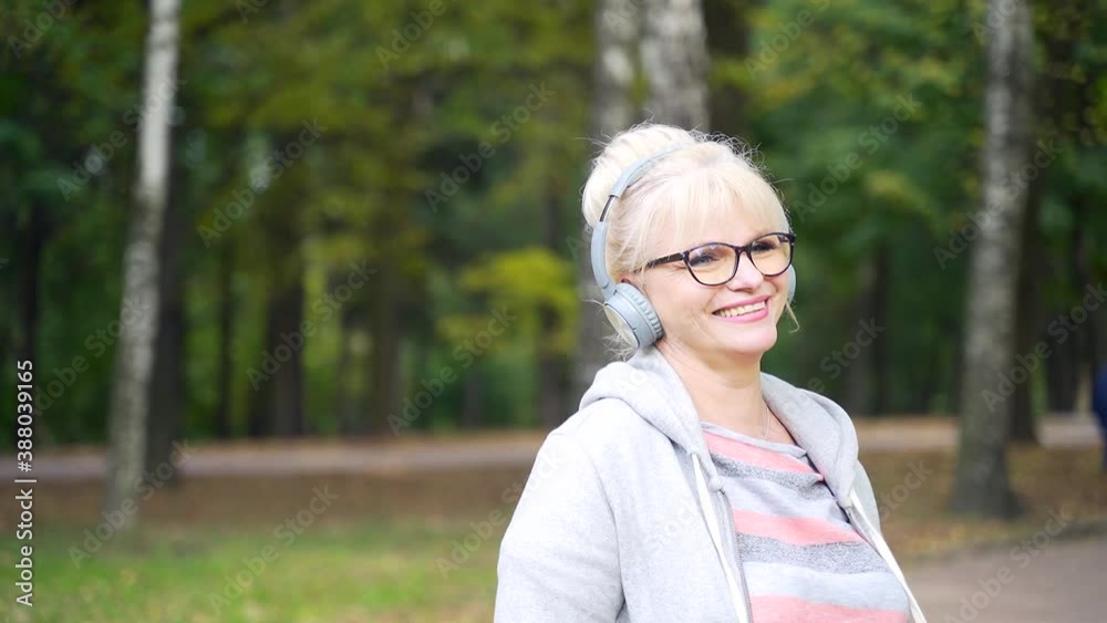 Senior Active Woman Walks in the Park or Forest and Listens to Music on Headphones. Portrait Mature Female Relaxing in Nature. Rest and Calm Retired Woman Enjoys Life Outdoors. Leisure and Lifestyle Senior Active Woman Walks in the Park or Forest and Listens to Music on Headphones. Portrait Mature Female Relaxing in Nature. Rest and Calm Retired Woman Enjoys Life Outdoors. Leisure and Lifestyle