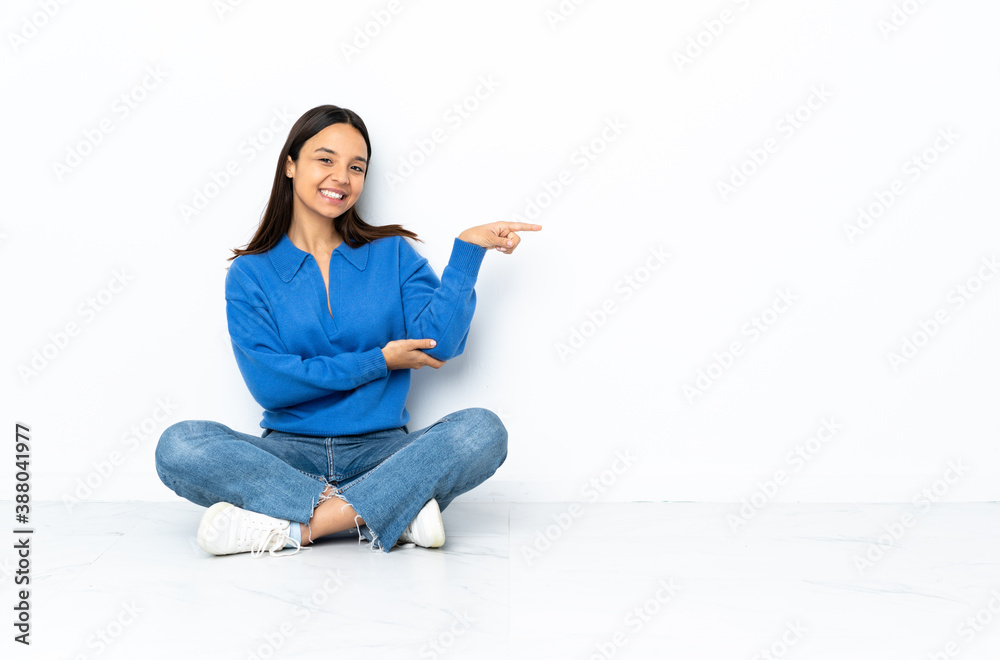 Young mixed race woman sitting on the floor isolated on white background pointing finger to the side Young mixed race woman sitting on the floor isolated on white background pointing finger to the side