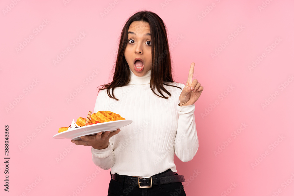 Young brunette woman holding waffles over isolated pink background thinking an idea pointing the finger up Young brunette woman holding waffles over isolated pink background thinking an idea pointing the finger up