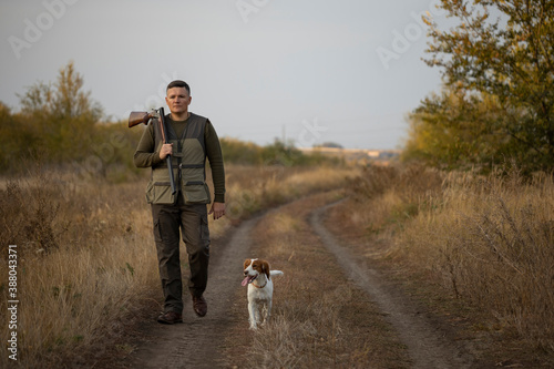 Hunter with Russian spaniel dog walking on the dirt road. Image taken during big game hunting trip. Hunting period, autumn season open. © kolidzei