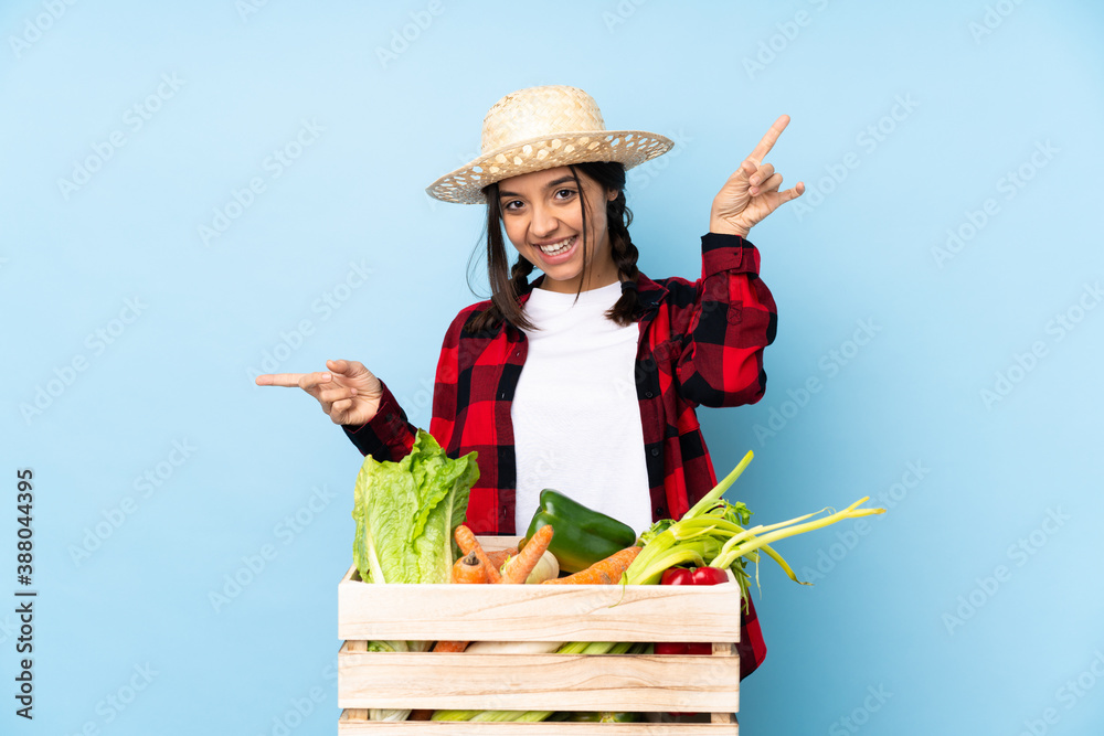 Young farmer Woman holding fresh vegetables in a wooden basket pointing finger to the laterals and happy