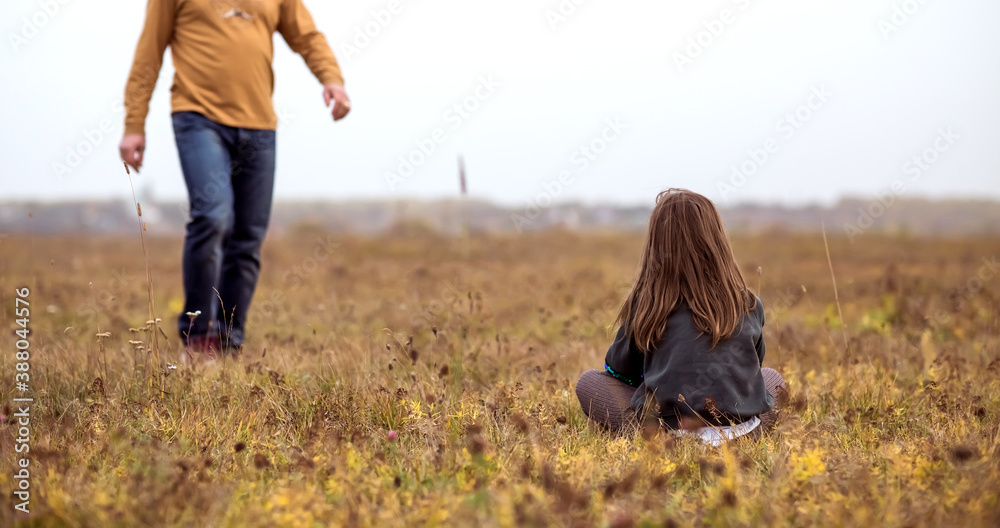 Father and daughter sitting on the grass in a field at sunset.