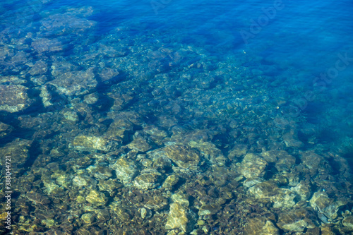 Clear crystal shallow blue sea water and rocky seabed background, high angle view.
