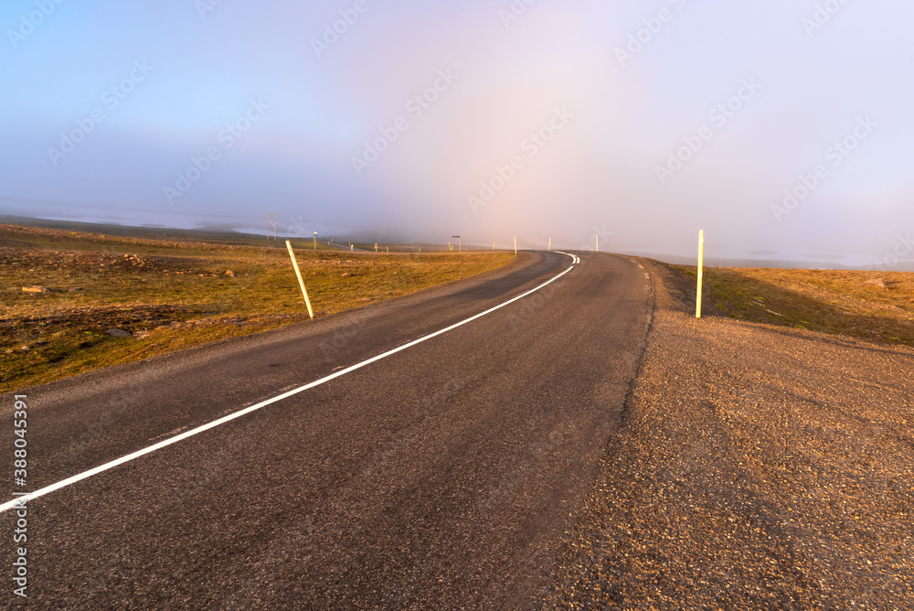 Empty winding mountain road covered with fog at sunset