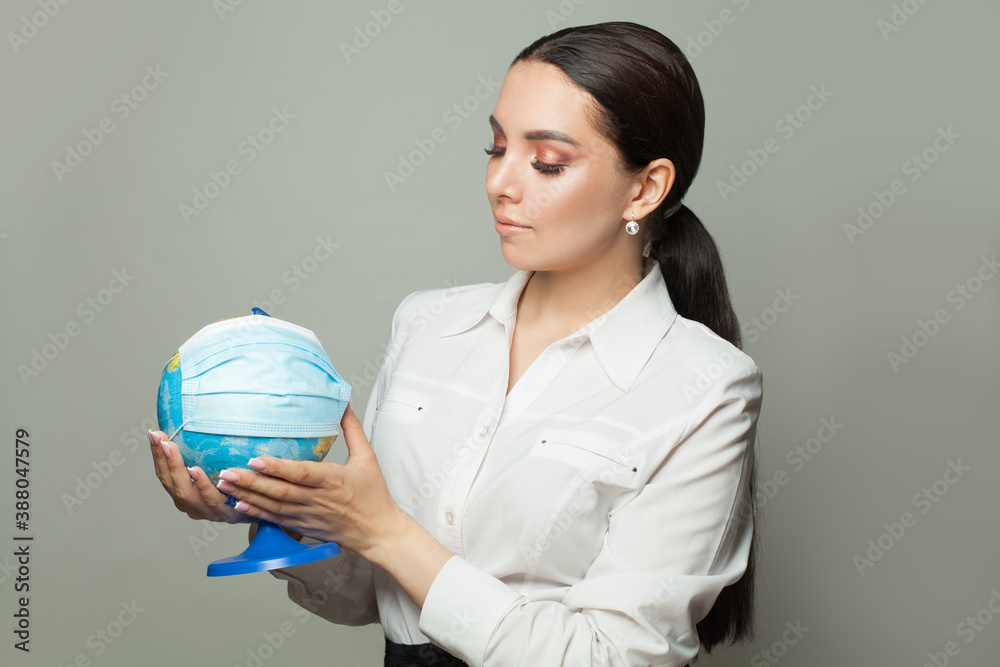 Global pandemic covid-19 concept. Caring woman with globe earth in medical protective mask on gray background Global pandemic covid-19 concept. Caring woman with globe earth in medical protective mask on gray background