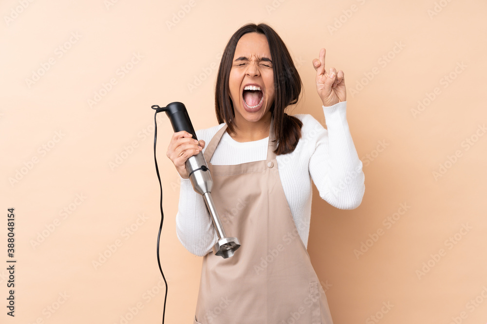 Young brunette girl using hand blender over isolated background with fingers crossing Young brunette girl using hand blender over isolated background with fingers crossing
