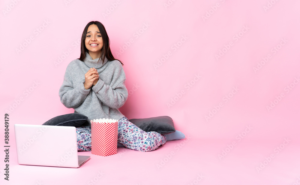 Young mixed race woman eating popcorn while watching a movie on the laptop laughing Young mixed race woman eating popcorn while watching a movie on the laptop laughing