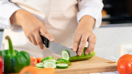 young Asian woman is preparing healthy food vegetable salad by Cutting cucumber for ingredients on cutting board on light kitchen, Cooking At Home and healthy food concept.