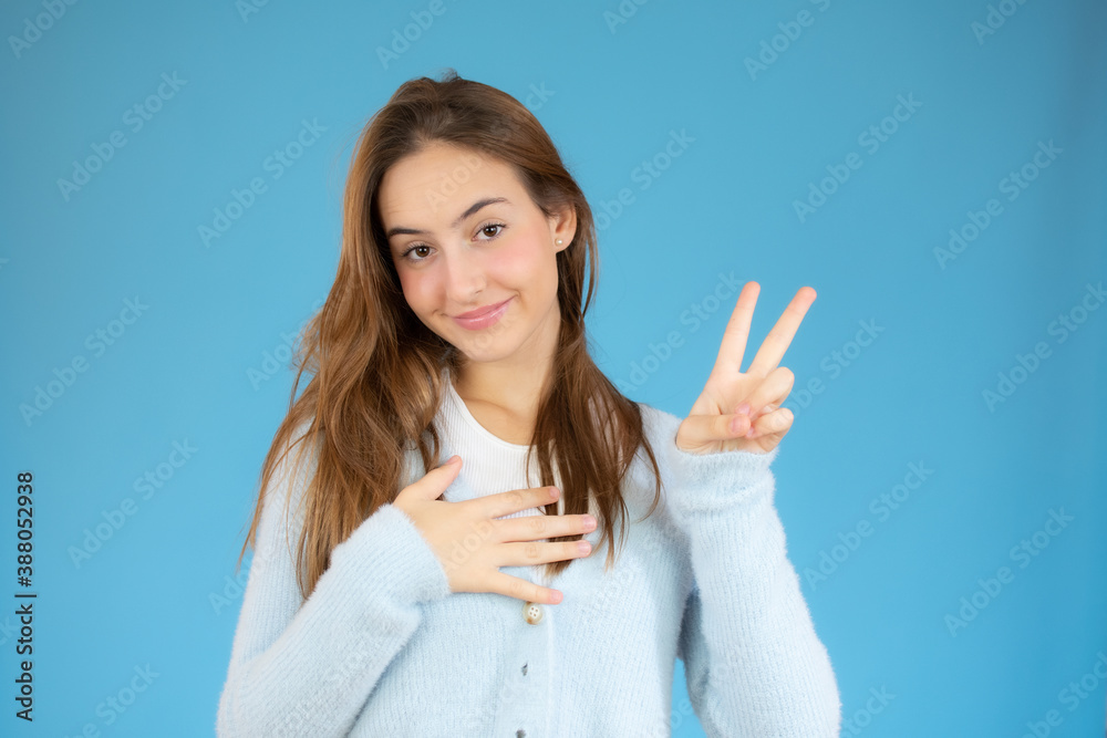 Portrait of a smiling happy woman showing victory sign and looking at camera isolated on the blue background Portrait of a smiling happy woman showing victory sign and looking at camera isolated on the blue background