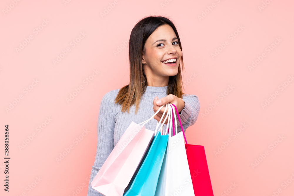 Woman over isolated pink background holding shopping bags and giving them to someone