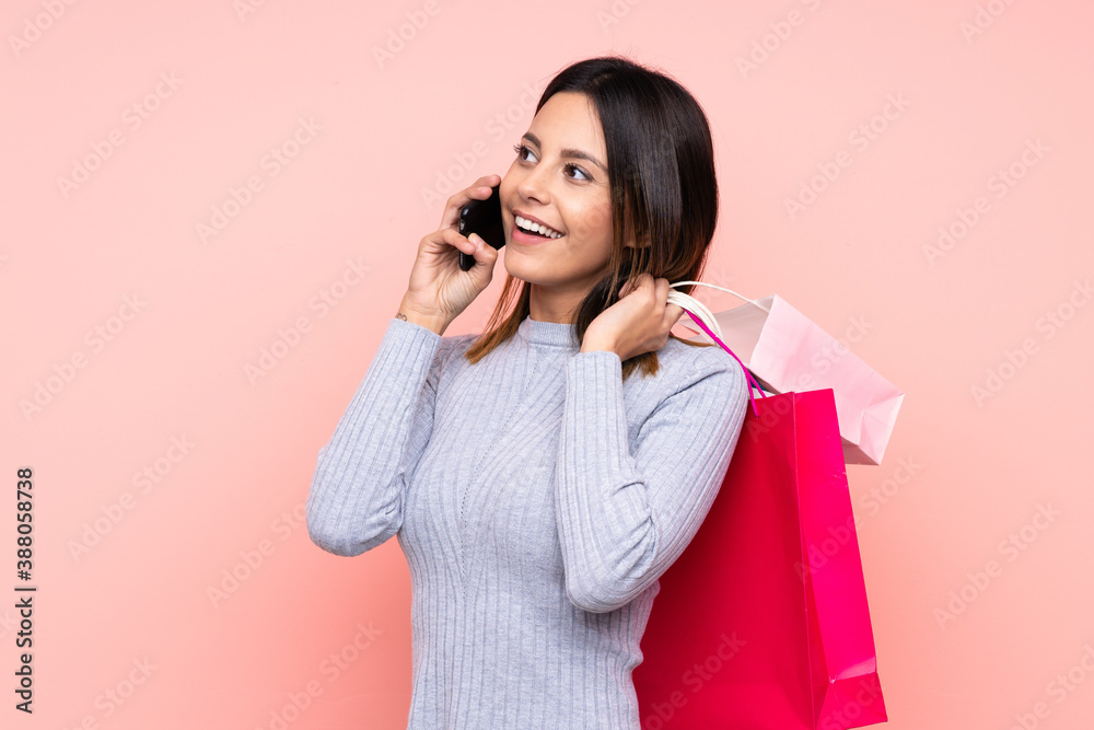 Woman over isolated pink background holding shopping bags and calling a friend with her cell phone Woman over isolated pink background holding shopping bags and calling a friend with her cell phone