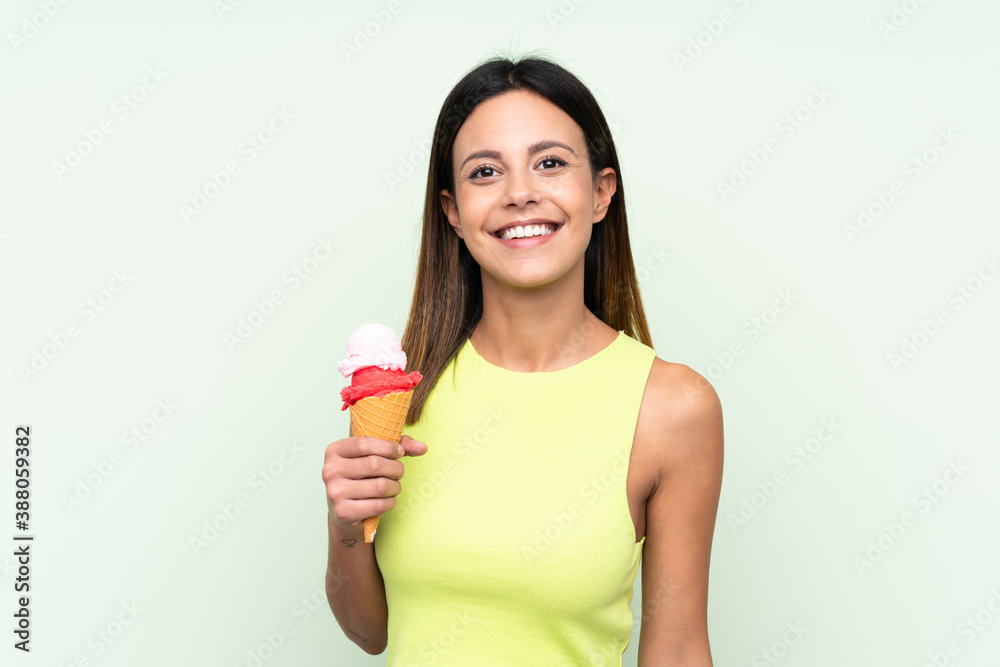 Brunette woman holding a cornet ice cream over isolated green background smiling a lot Brunette woman holding a cornet ice cream over isolated green background smiling a lot