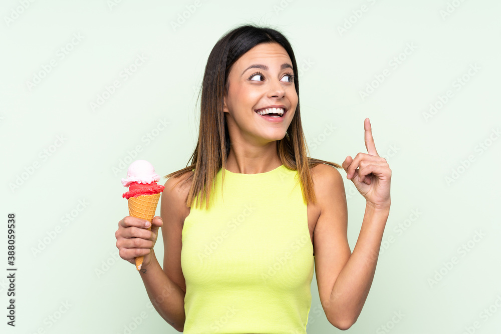Brunette woman holding a cornet ice cream over isolated green background intending to realizes the solution while lifting a finger up Brunette woman holding a cornet ice cream over isolated green background intending to realizes the solution while lifting a finger up
