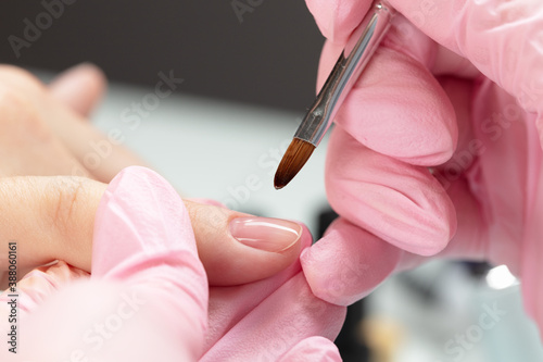 Process of applying transparent varnish. Woman in salon receiving manicure by nail beautician. Clear Nail polish and brush  macro.
