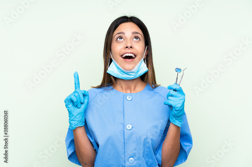 Woman dentist holding tools over isolated green background pointing with the index finger a great idea