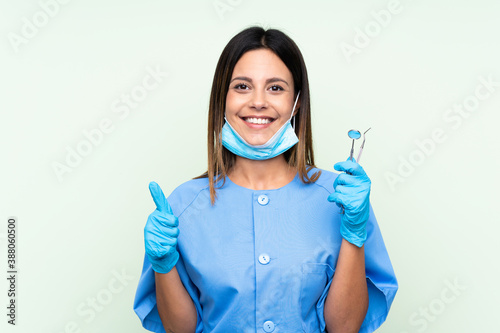 Woman dentist holding tools over isolated green background giving a thumbs up gesture