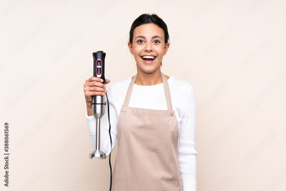 Woman using hand blender over isolated background with surprise and shocked facial expression