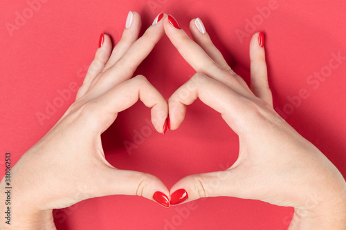 Beautiful hands of a young woman making sign Heart by fingers on red background. Female hands showing gesture after receiving cosmetic services from a beautician. Love concept on Valentine day.