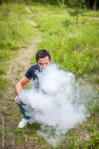 Confident man smokes electronic cigarette exhales smoke on the forest floor. Alternative to smoking.