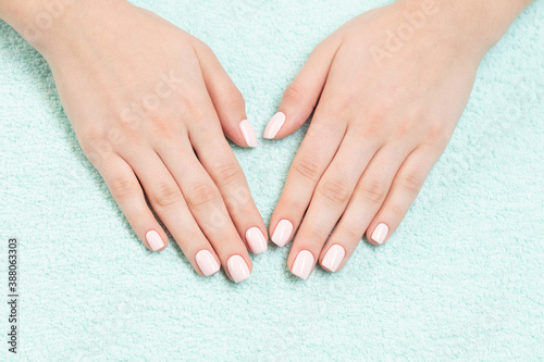 Female hands with new manicure. Hands with pink nail polish on a colored towel. Care for woman hands. Woman in salon receiving manicure by nail beautician.
