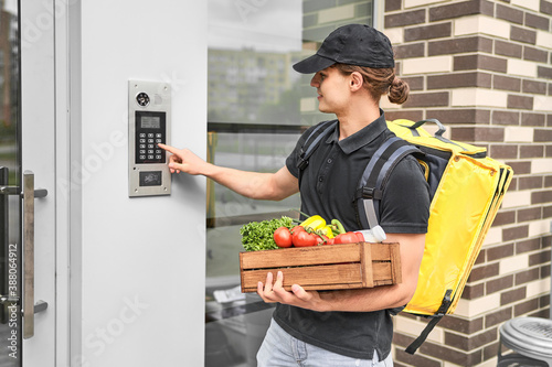 .A man courier with a backpack and vegetables in his hands calls the intercom to deliver the order to the customer online photo