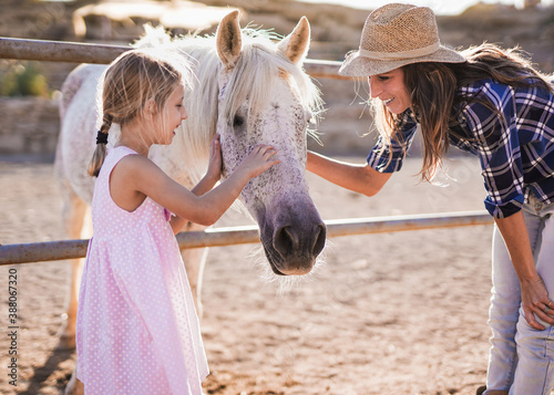 Canvas Print Happy mother and daughter caress horse outdoor at ranch - Mom and child - Animal