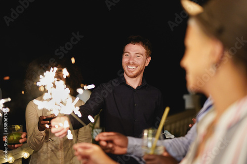 Happy multiracial friends with cocktails and sparklers firework - Young people celebrate together outdoor
