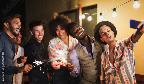 Fotografia Happy multiracial friends celebrate outdoor with sparkler firework and taking a