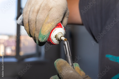 worker lubricates the iron drill of the drill with oil technical lubricant, maintenance of tools