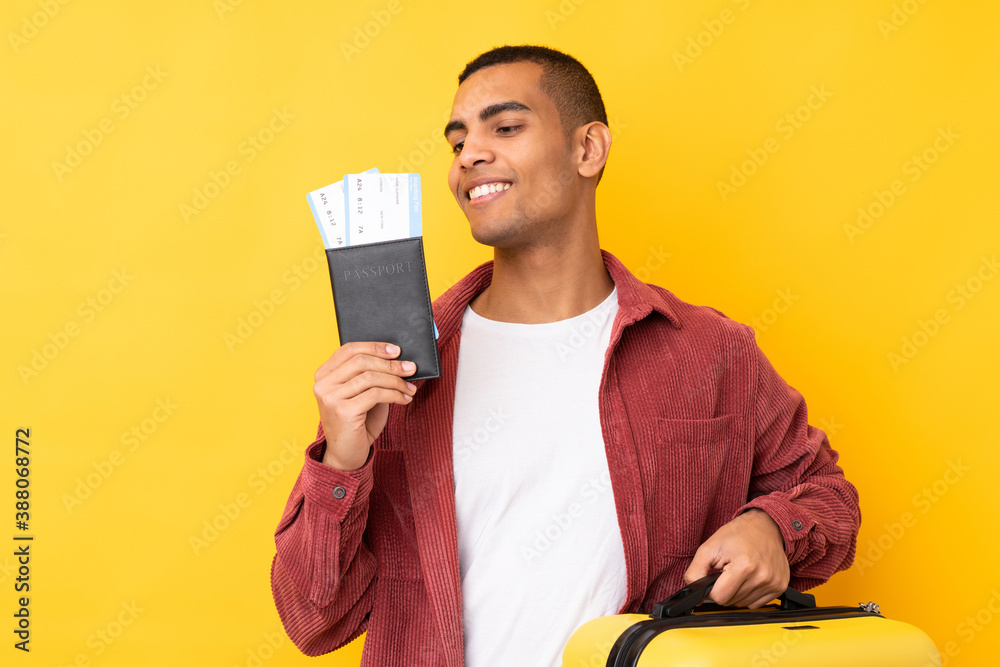 Young African American man over isolated yellow background in vacation with suitcase and passport