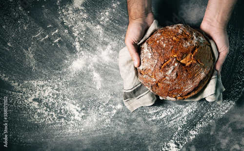 Photographie Baker's hands holding and presenting fresh baked loaf of bread